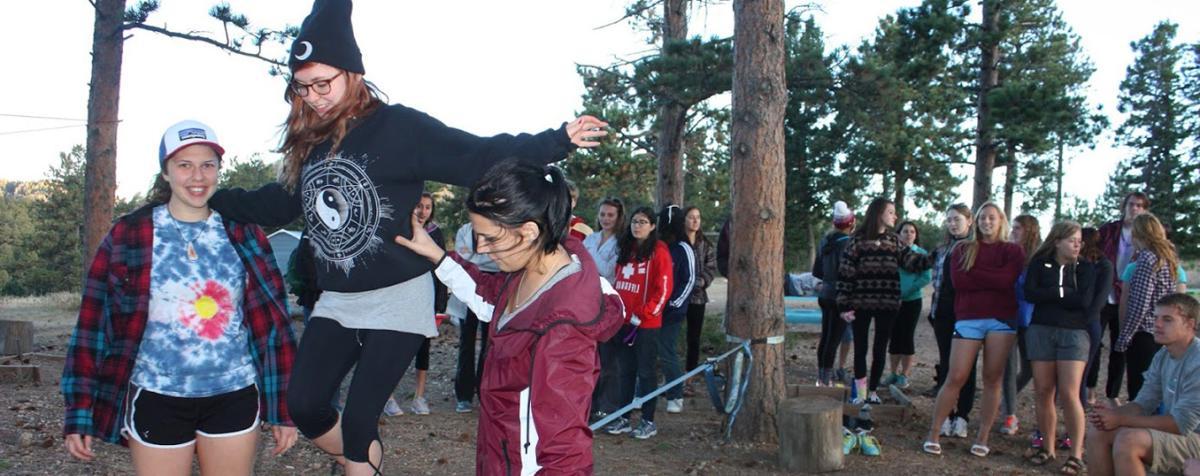 two students helping one student walk tightrope in forrest 